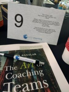A photo showing a copy of the book 'The Art of Coaching Teams', a pen, and a table tent that includes a quote from Rumi.