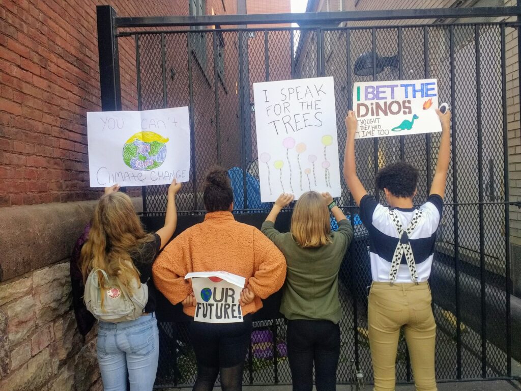 Four students facing backwards holding signs, confronting climate change