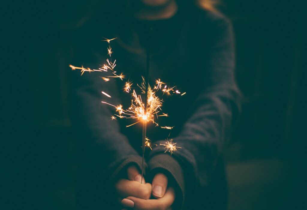 cupped hands in darkness, holding a lit sparkler