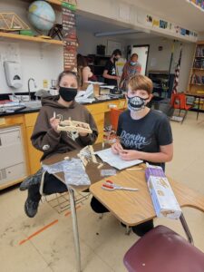 Two masked students work together at a pair of desks