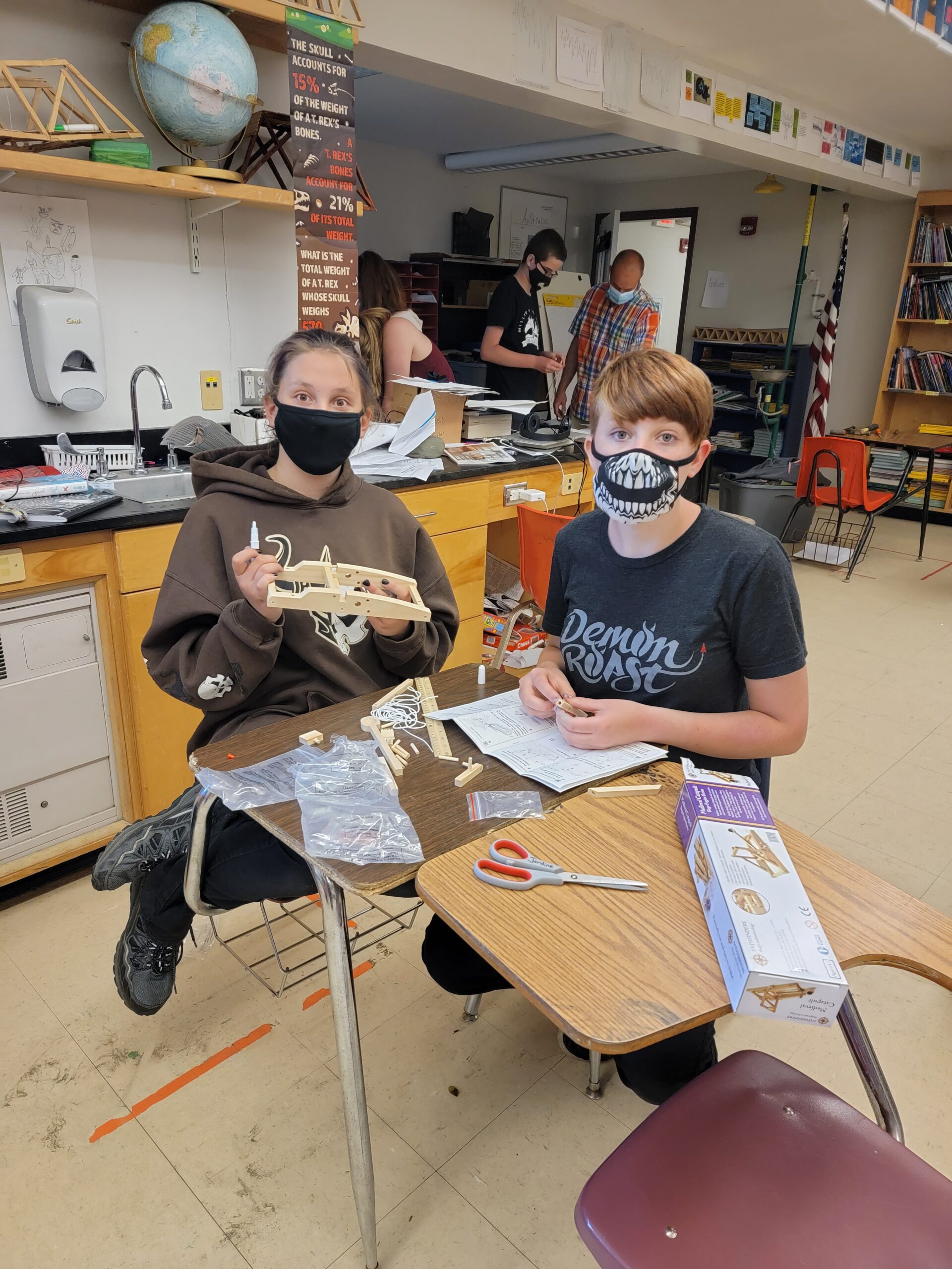 Two masked students work together at a pair of desks