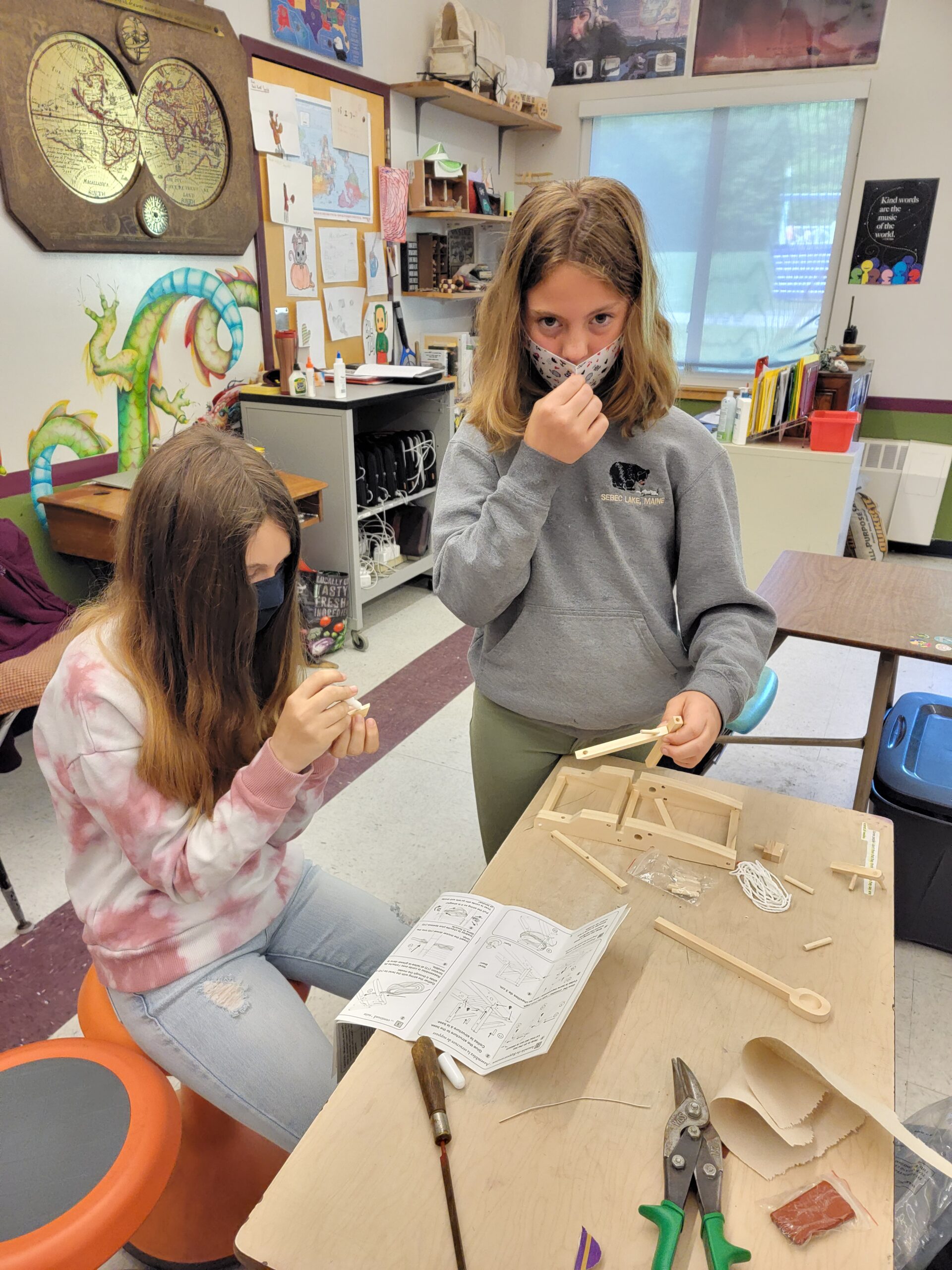 A student adjusts their cloth mask while another masked student works nearby