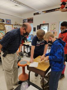 A masked instructor looks at work being done by two masked students