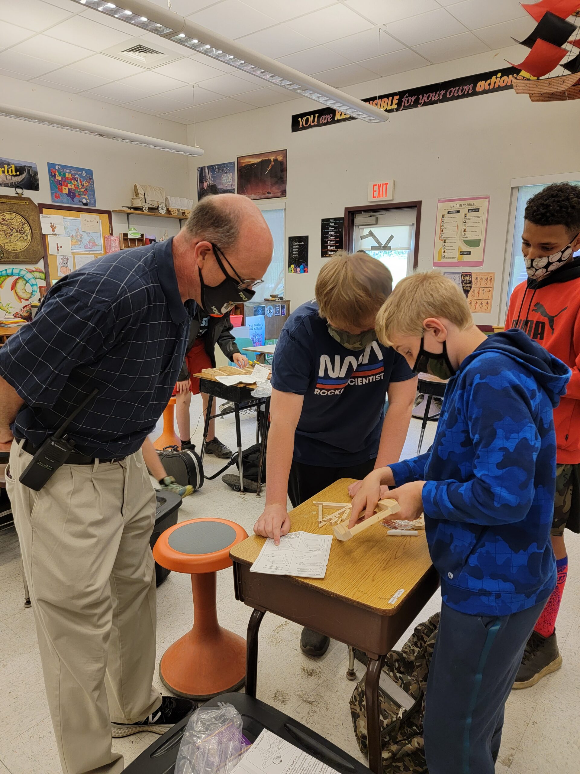 A masked instructor looks at work being done by two masked students