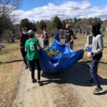 A group of students holds a huge pile of leaves in a blue tarp