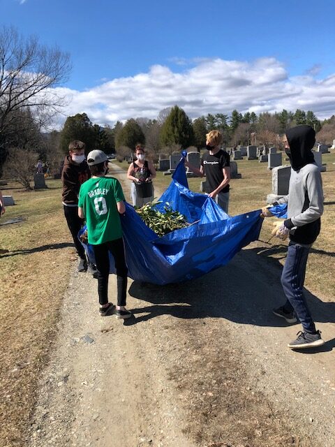 A group of students holds a huge pile of leaves in a blue tarp