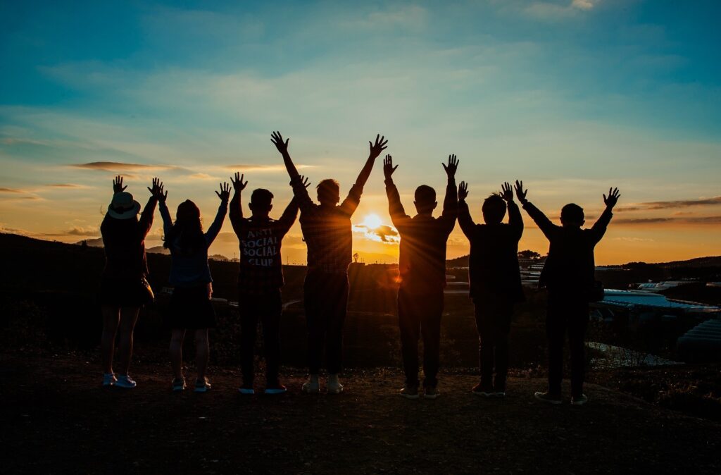 A group of people in silhouette raise their hands to the sunset