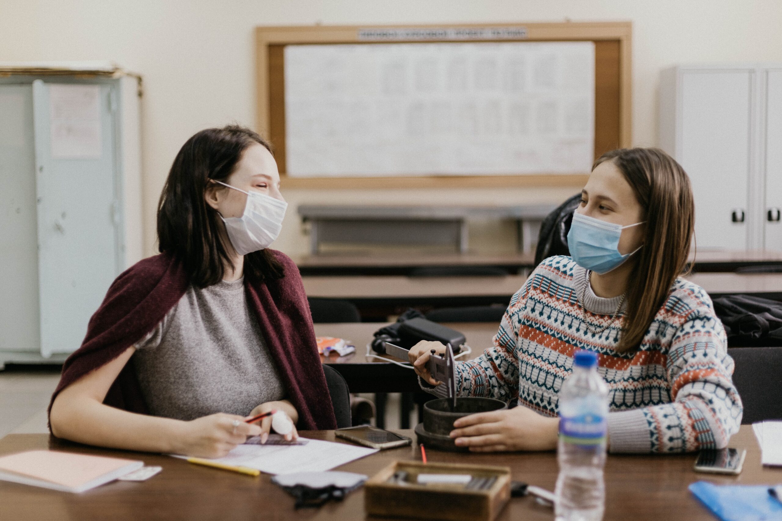 Two masked women sit chatting in an office