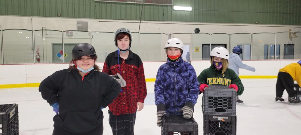 A group of masked students in helmets pose for a photo on an ice rink