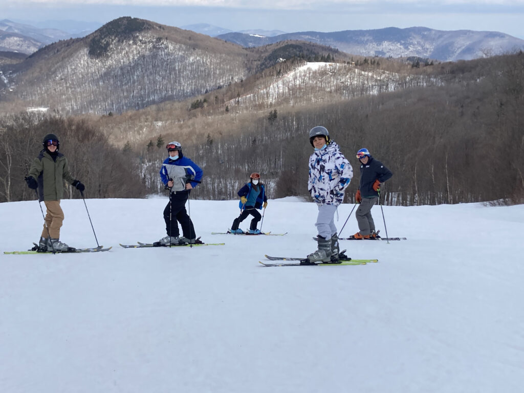 Five students on skis and with masks and helmets pose for a photo against a dramatic mountain backdrop