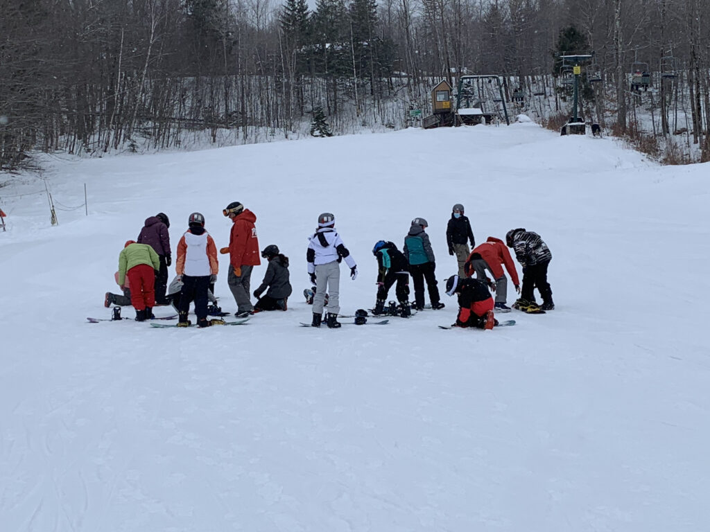 A group of students gather on skis and in winter gear, preparing to go out skiing