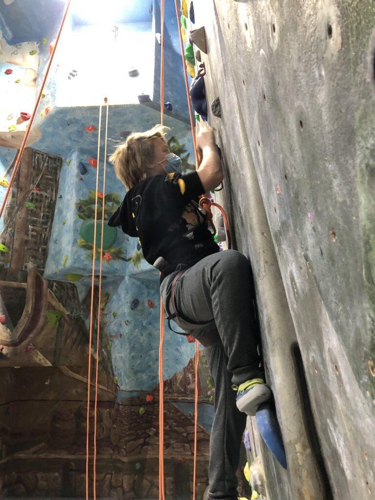 A masked student climbs on a climbing wall