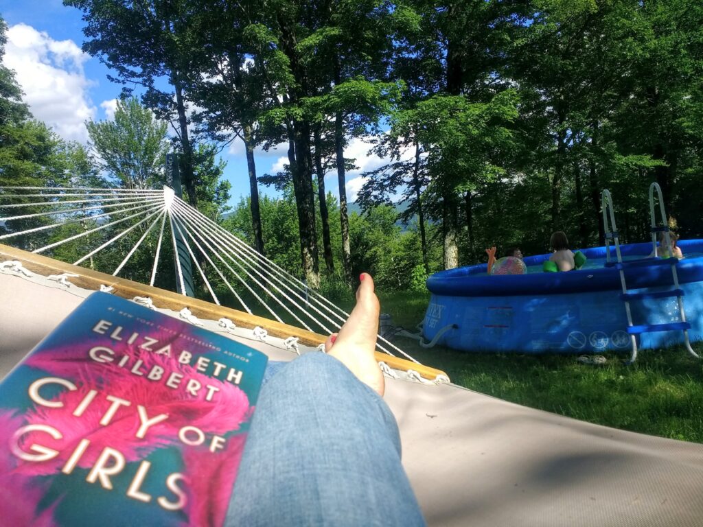 Feet in a hammock, next to a swimming pool in a shady glen.