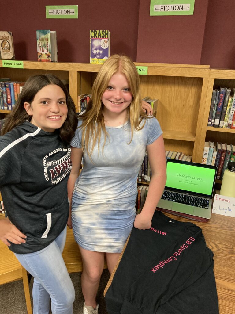 Two students pose by a laptop