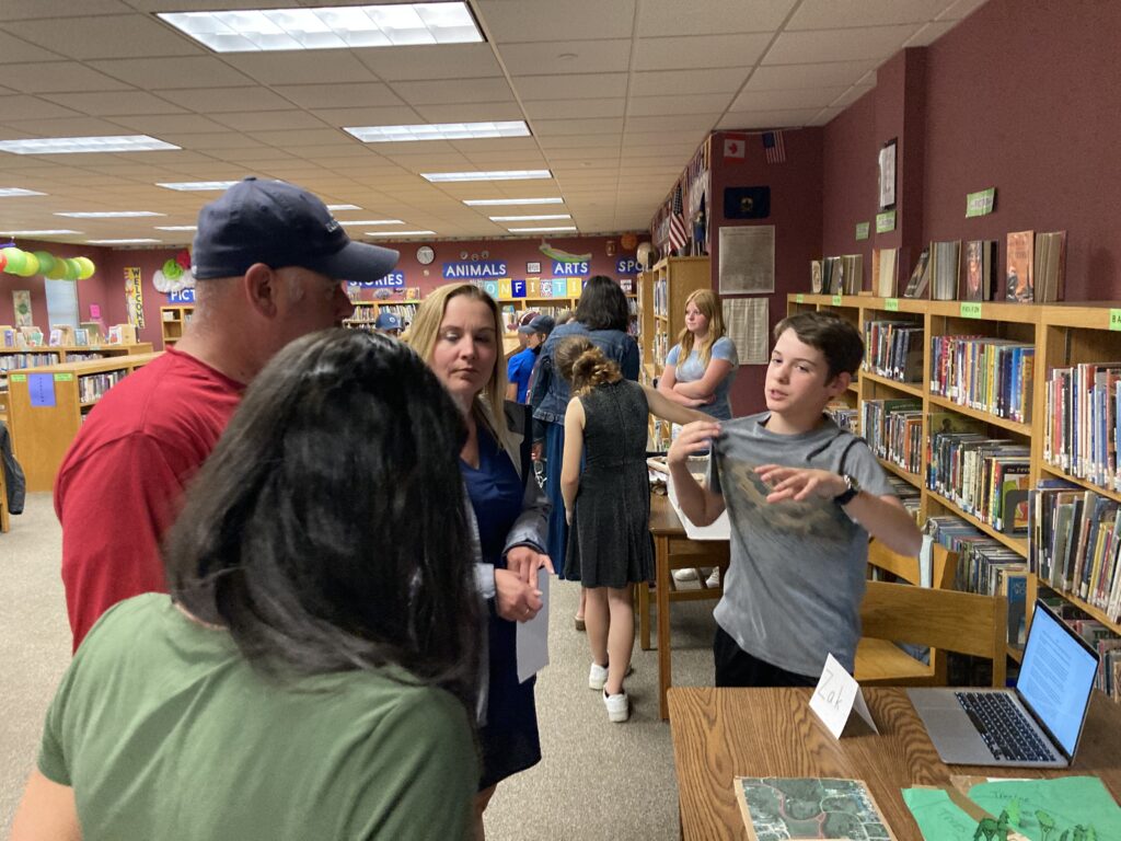 A student explains their project to two adults