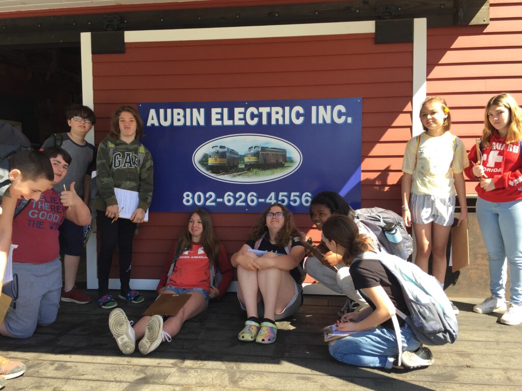 A group of students stand next to a sign advertising a business