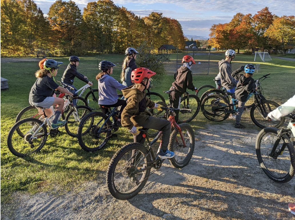 Students on mountain bikes with soccer goal in the background.