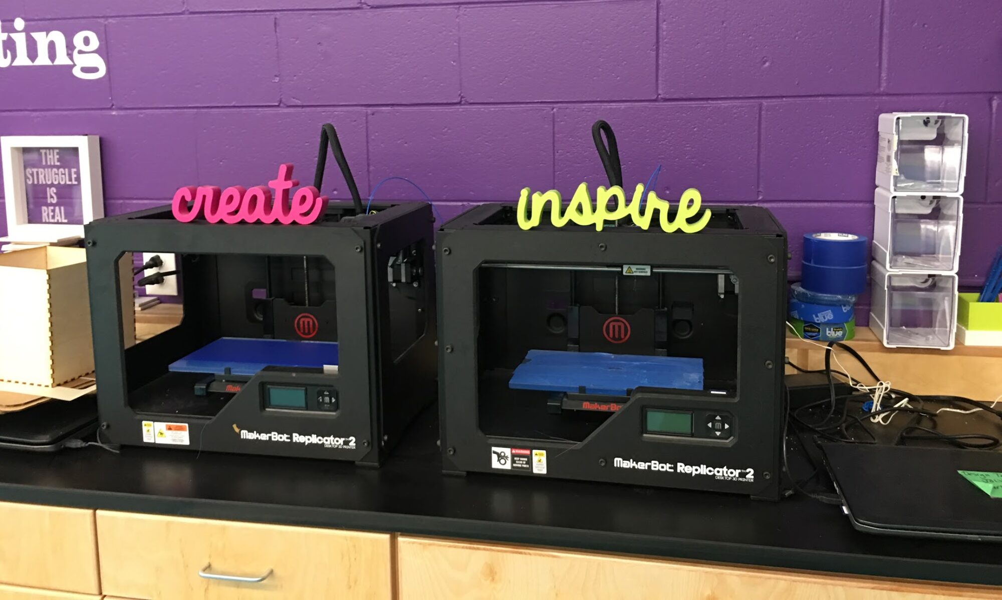 Two 3D printers in a makerspace, one labeled "create" the other labeled "inspire"